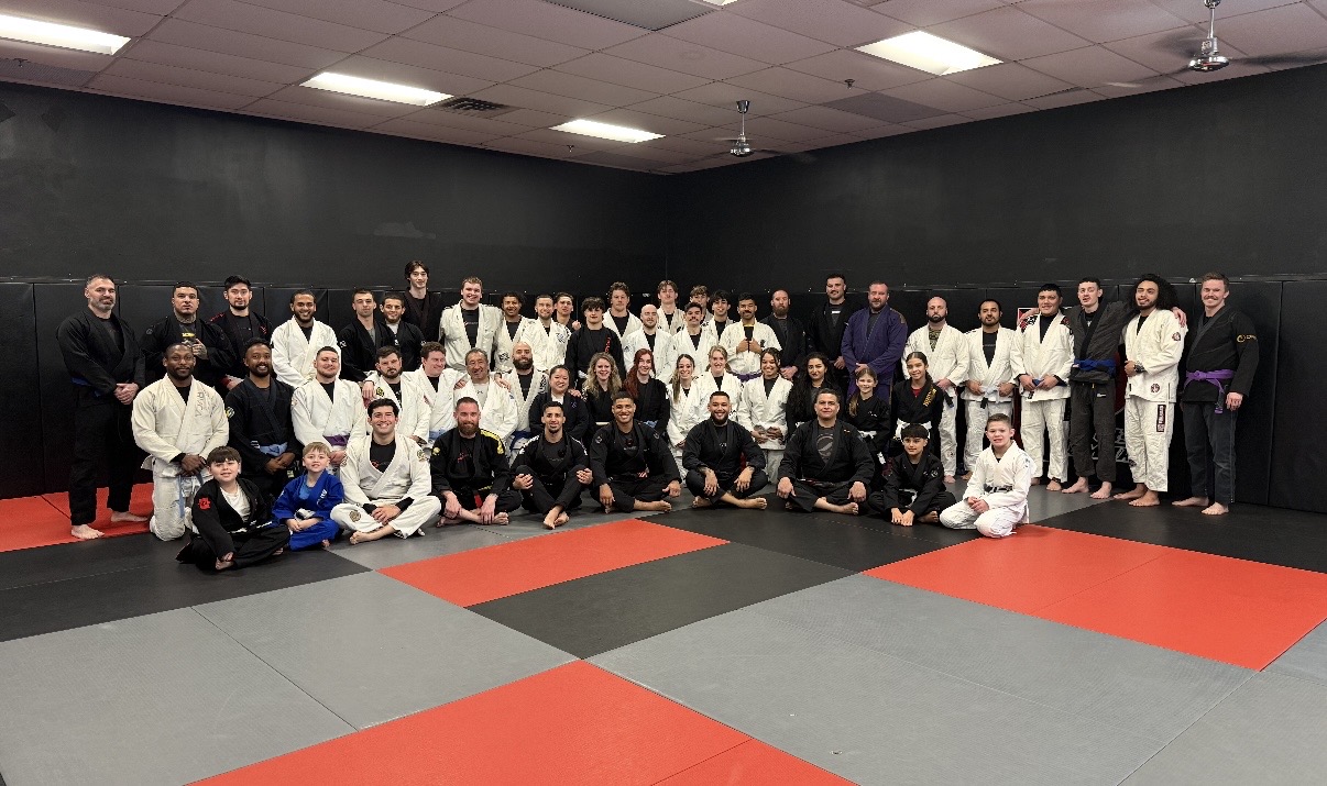 Full class of adults and kids in gis gathered on the academy mats after training